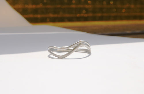 Silver ring with a wavy design on a white surface