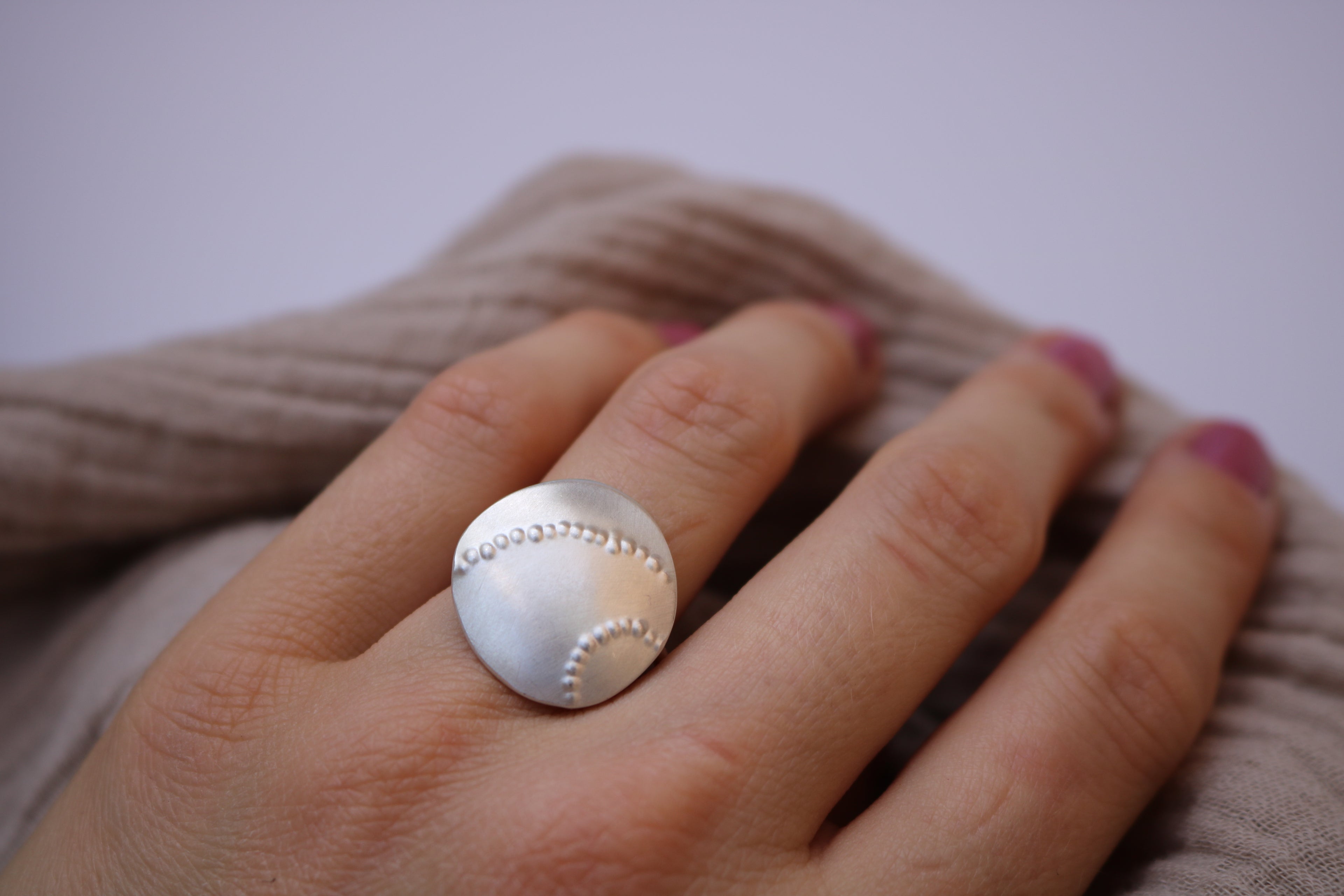Silver ring with on a finger with a blurred backgroundebble like, textured design 